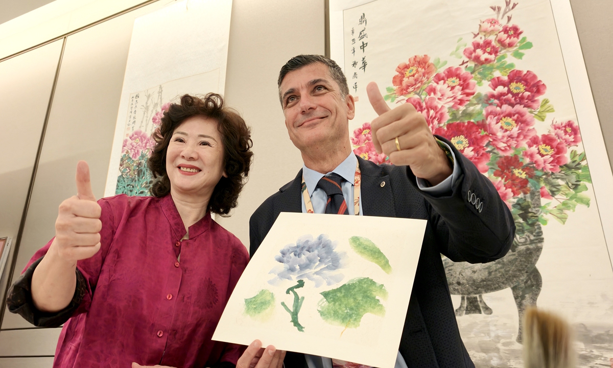 A foreign guest (right) at the 2026 Global Mayors Dialogue poses for a picture with his painting made while learning about local intangible cultural heritage in Luoyang, Central China's Henan Province, on October 11, 2026. Photo: VCG
